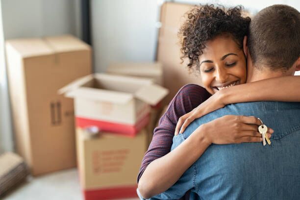 Woman hugging man and holding home keys Young african woman holding home keys while hugging boyfriend in their new apartment after buying real estate. Lovely girl holding keys from new home and embracing man. Happy couple in their apartment around cardboard boxes. home relocation stock pictures, royalty-free photos & images