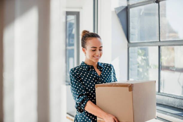 Unloading New Office Supplies Woman laughing and looking down while carrying a cardboard box at work. moving company stock pictures, royalty-free photos & images