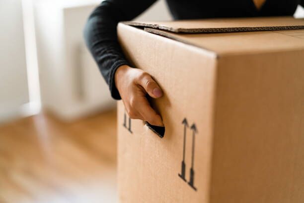 Woman carrying boxes into her new home A woman is carrying cardboard moving boxes into her new apartment. movers carrying boxes stock pictures, royalty-free photos & images