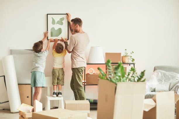 Hanging Picture Together Full length portrait of happy father with two sons hanging pictures on wall while moving in to new home, copy space moving to a new home stock pictures, royalty-free photos & images