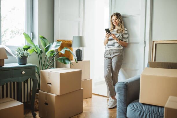 Mature woman with Moving Boxes in New Home Mature woman moves in to new home, unpacking boxes and enjoying in her new home. She is resting and using smart phone. movers stock pictures, royalty-free photos & images