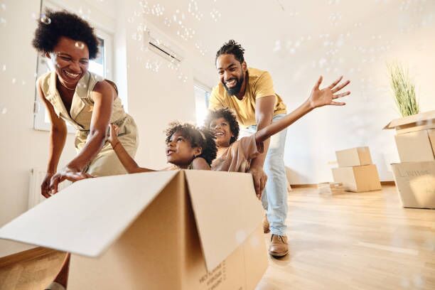 Carefree black family having fun after moving into a new home. Playful African American parents having fun while pushing their small kids in carboard box at new apartment. Copy space. packing boxes stock pictures, royalty-free photos & images