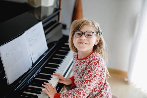 Little happy girl playing piano in living room. Cute preschool child with eye glasses having fun with learning to play music instrument. Little happy girl playing piano in living room. Cute preschool child with eye glasses having fun with learning to play music instrument piano movement stock pictures, royalty-free photos & images