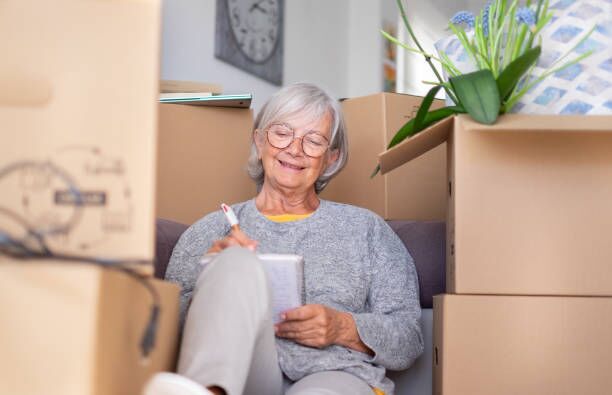 Happy senior woman involved in moving house sitting among cardboard boxes making note of purchases and to-dos, concept of moving, retirement, new life, buying, renting, apartment, house Happy senior woman involved in moving house sitting among cardboard boxes making note of purchases and to-dos, concept of moving, retirement, new life, buying, renting, apartment, house moving to new home stock pictures, royalty-free photos & images