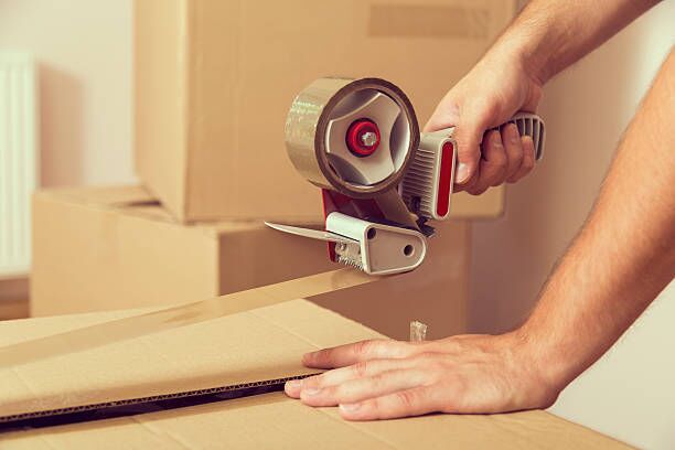 Packing Close up of a guy’s hands holding packing machine and sealing cardboard boxes with duct tape moving company stock pictures, royalty-free photos & images