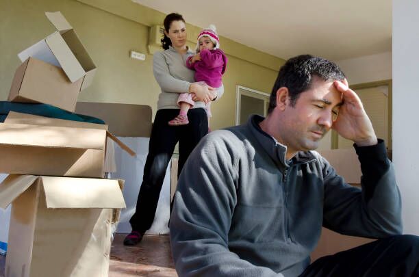 Concept Photo - Divorce, Eviction, Financial or Family Issues Young parents and their daughter stand beside cardboard boxes outside their home. Concept photo illustrating divorce, homelessness, eviction, unemployment, financial, marriage or family issues. moving stress stock pictures, royalty-free photos & images