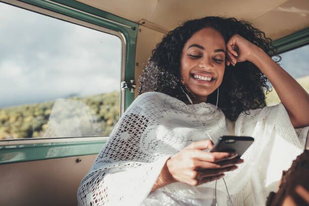 Woman enjoying on her road trip African woman on road trip travelling by van. Smiling female sitting on backseat of car and  listening music with mobile phone. traveling with music stock pictures, royalty-free photos & images
