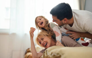 A man and woman lying on a bed with a child on her shoulders. They just moved in with Apartment movers in Dallas.